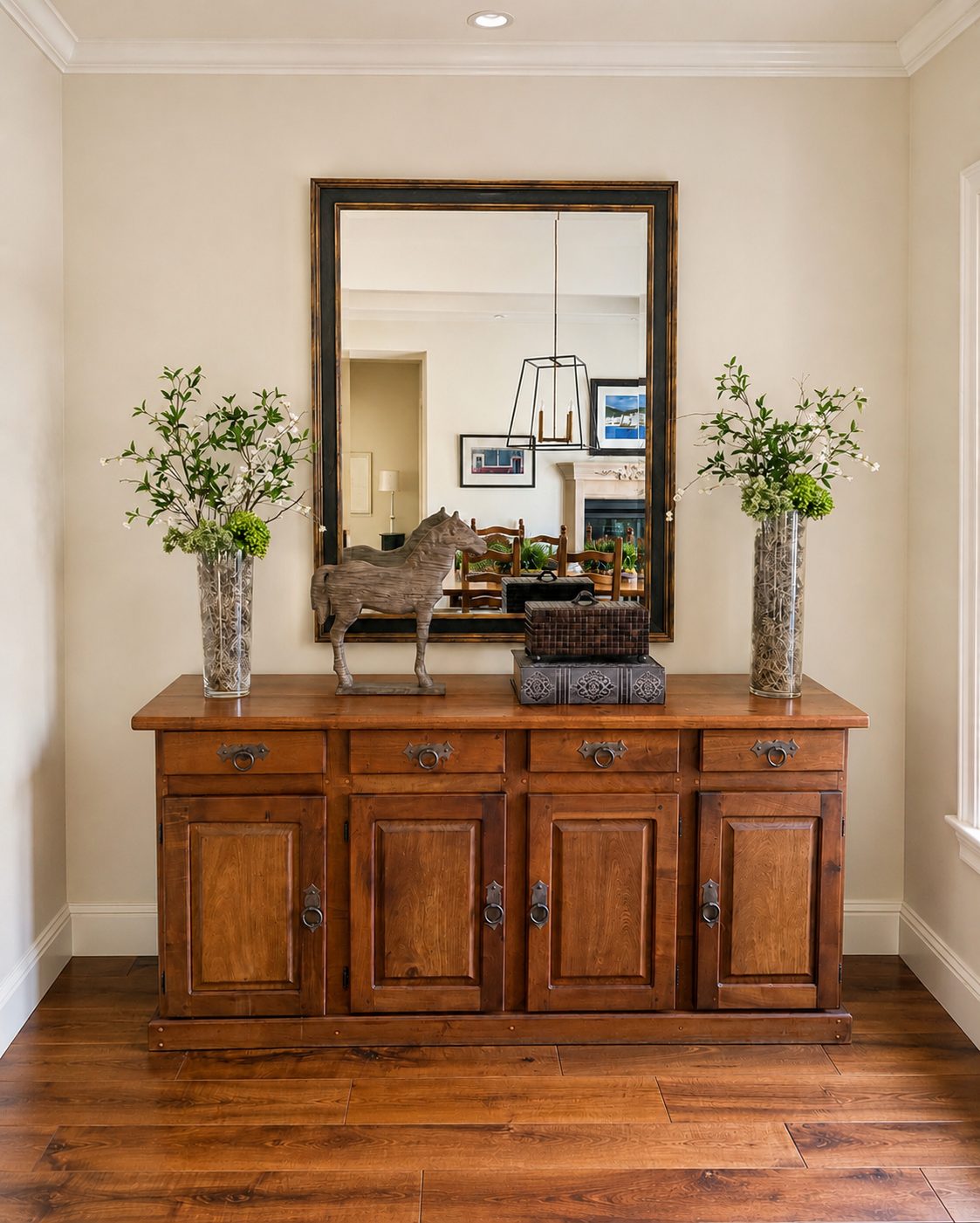 Entry with a carved wood console, framed mirror, greenery in tall vases and a horse sculpture