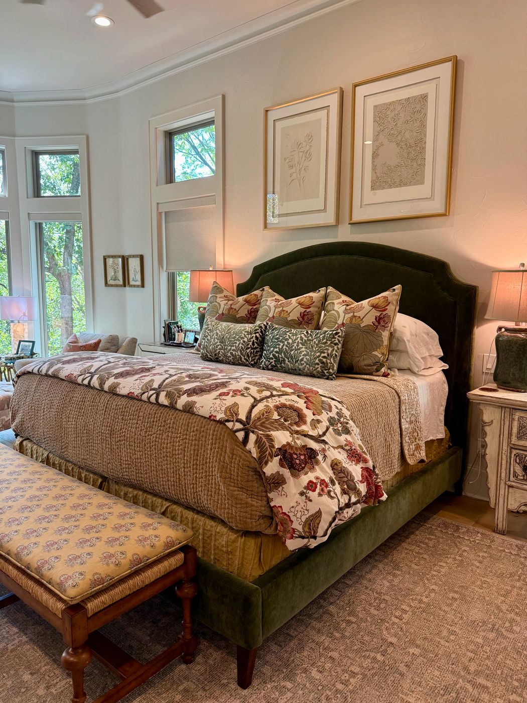Southlake bedroom with a green velvet upholstered bed, layered floral bedding and framed botanical prints